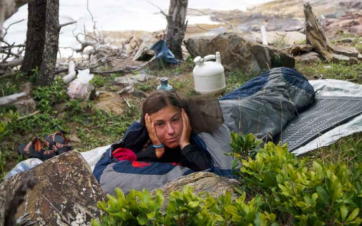 a student rests on a sleeping pad near the shore on an outward bound expedition in maine